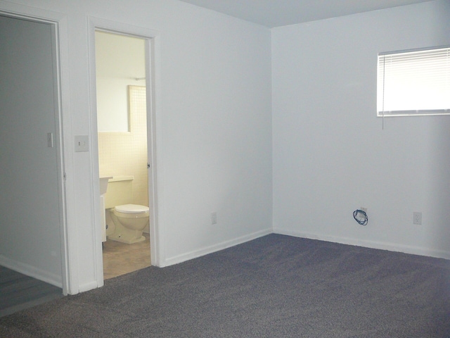 unfurnished bedroom with dark colored carpet and connected bathroom