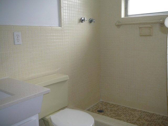 bathroom with toilet, vanity, tile walls, and tiled shower