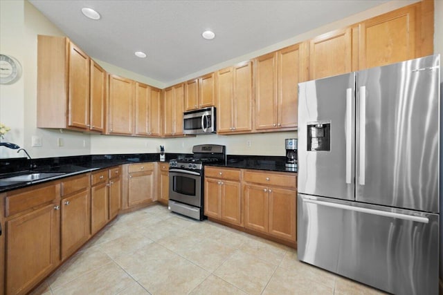 kitchen featuring appliances with stainless steel finishes, light tile patterned floors, dark stone countertops, and sink