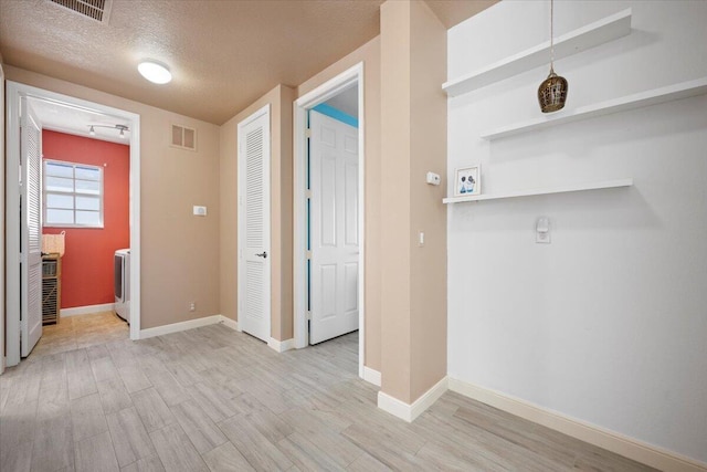 hall featuring washer / dryer, a textured ceiling, and light hardwood / wood-style flooring