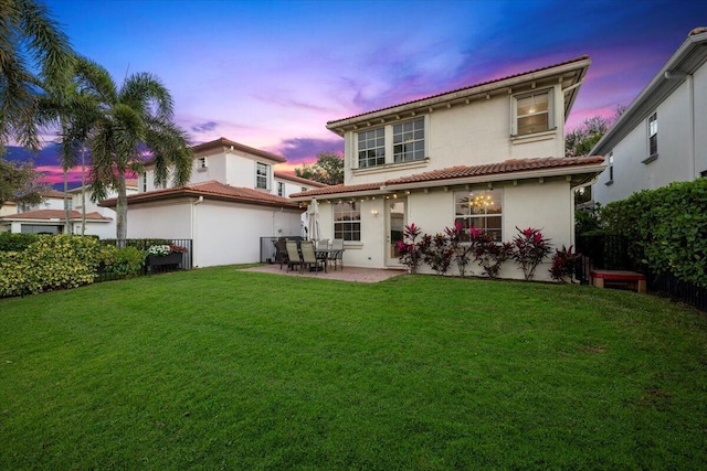 back house at dusk with a lawn and a patio area