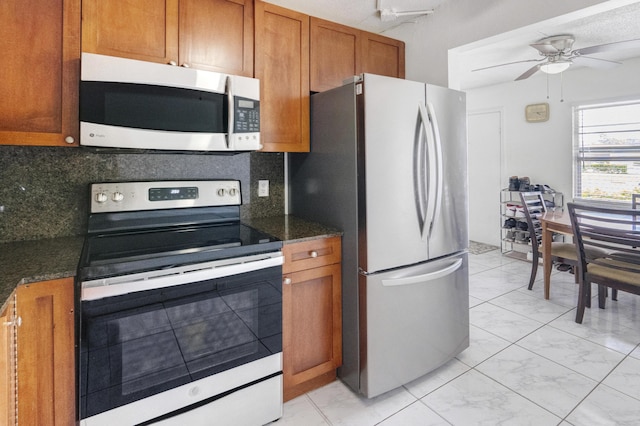 kitchen with backsplash, ceiling fan, dark stone counters, and appliances with stainless steel finishes