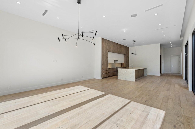 unfurnished living room with visible vents, a sink, baseboards, and light wood finished floors