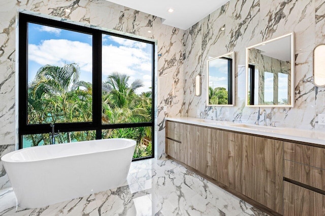 bathroom with a sink, marble finish floor, stone wall, and a soaking tub