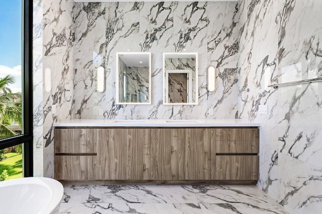 bathroom with a freestanding tub, stone wall, a sink, and marble finish floor