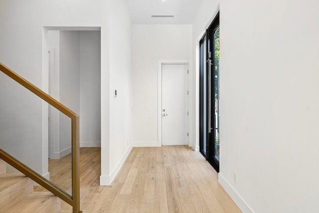 hall with light wood-style floors, stairs, and baseboards