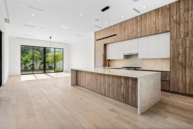 kitchen with decorative backsplash, modern cabinets, white cabinets, light wood finished floors, and under cabinet range hood