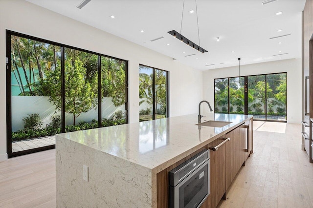 kitchen with modern cabinets, light wood-type flooring, a sink, light stone counters, and stainless steel microwave