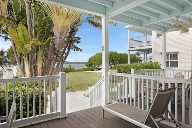 wooden terrace with ceiling fan, a lawn, and a water view