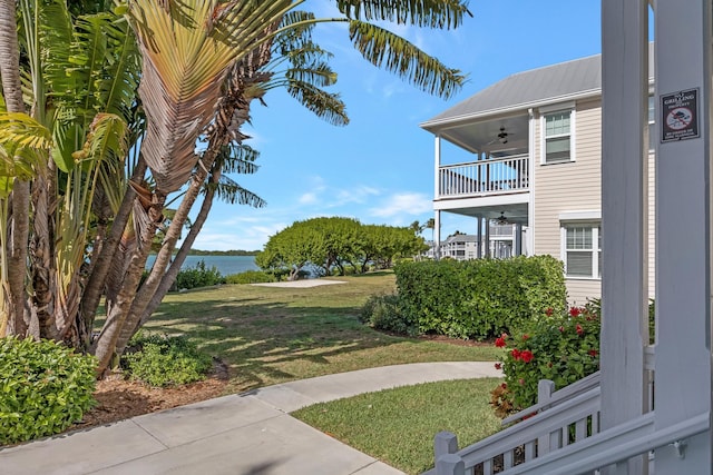 view of yard with ceiling fan, a water view, and a balcony