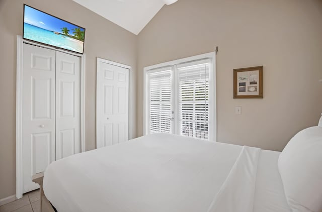 tiled bedroom featuring multiple closets and vaulted ceiling