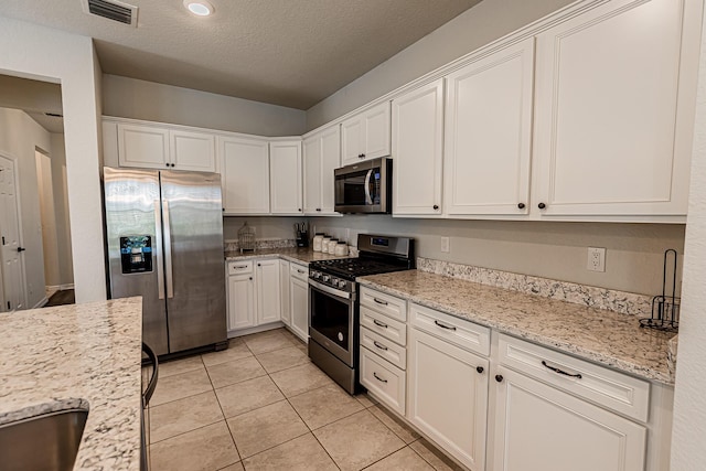 kitchen with light stone countertops, appliances with stainless steel finishes, light tile patterned floors, and white cabinets