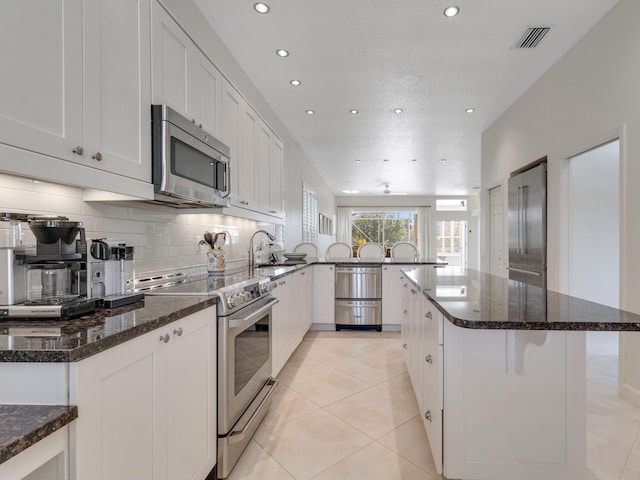 kitchen featuring dark stone countertops, a center island, white cabinets, and appliances with stainless steel finishes