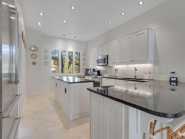 kitchen with dark stone counters, white cabinets, sink, appliances with stainless steel finishes, and a kitchen island