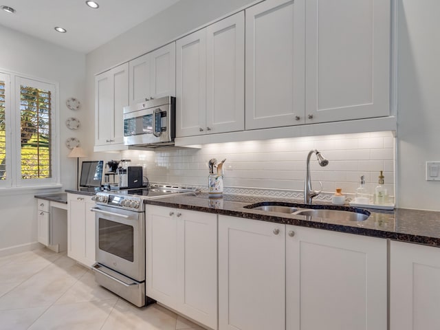 kitchen with white cabinetry, sink, stainless steel appliances, dark stone counters, and decorative backsplash