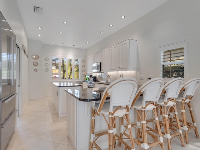 kitchen with a breakfast bar, white cabinets, dark stone countertops, a kitchen island, and stainless steel appliances