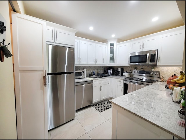 kitchen featuring white cabinetry, light stone counters, backsplash, light tile patterned floors, and appliances with stainless steel finishes