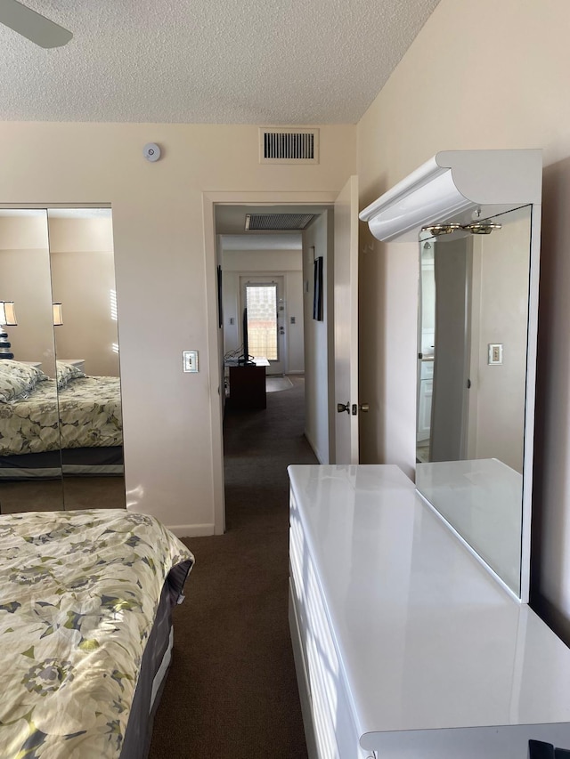 bedroom featuring ceiling fan, a closet, a textured ceiling, and dark colored carpet