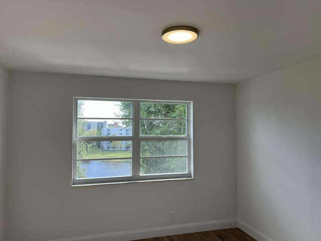 empty room with dark hardwood / wood-style floors, a healthy amount of sunlight, and a water view