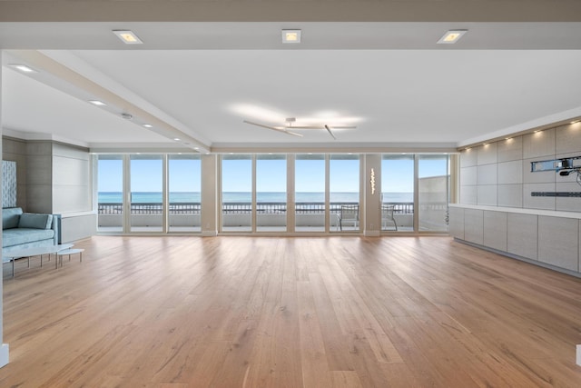 unfurnished living room with a wealth of natural light, floor to ceiling windows, ceiling fan, a water view, and light hardwood / wood-style floors