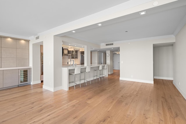 unfurnished living room featuring light hardwood / wood-style flooring, beverage cooler, ornamental molding, and sink