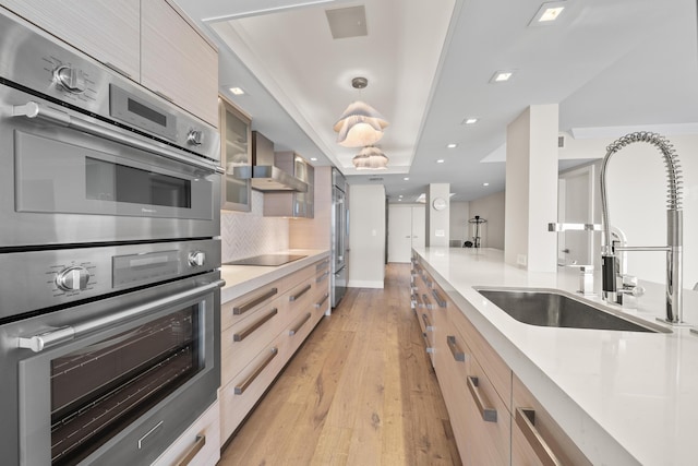 kitchen featuring light brown cabinetry, wall chimney exhaust hood, stainless steel double oven, sink, and light hardwood / wood-style floors