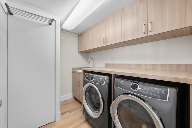 laundry area with washer and dryer, cabinets, light wood-type flooring, and sink