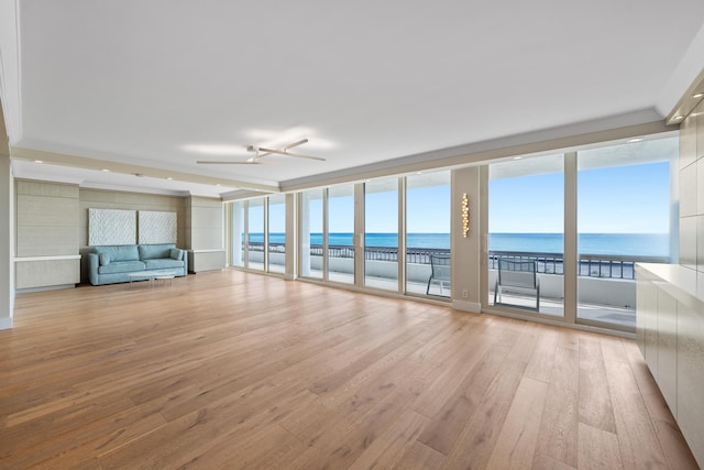 unfurnished living room featuring a wealth of natural light, ceiling fan, a water view, and light wood-type flooring