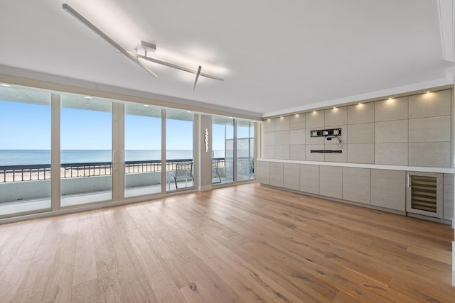 unfurnished living room featuring light hardwood / wood-style floors, a water view, a wall of windows, and a beach view