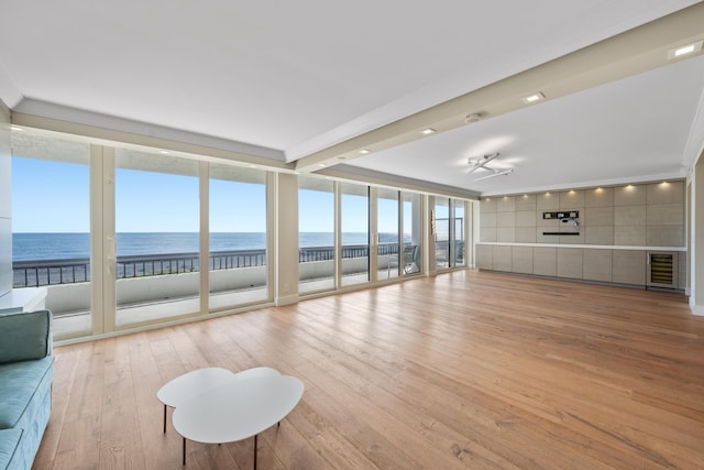 unfurnished living room with expansive windows, a water view, light hardwood / wood-style floors, and a beach view