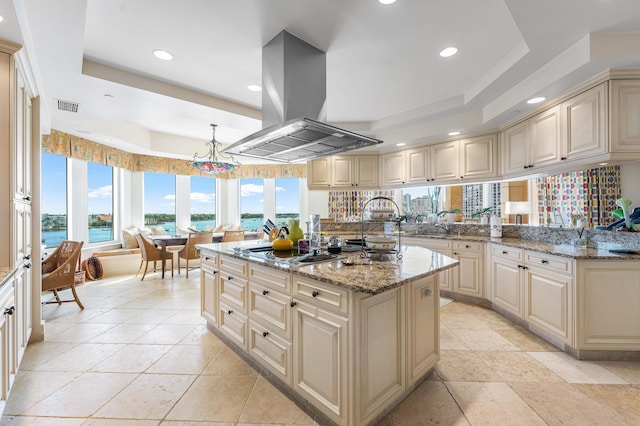 kitchen featuring cream cabinets, a tray ceiling, a center island with sink, and island exhaust hood