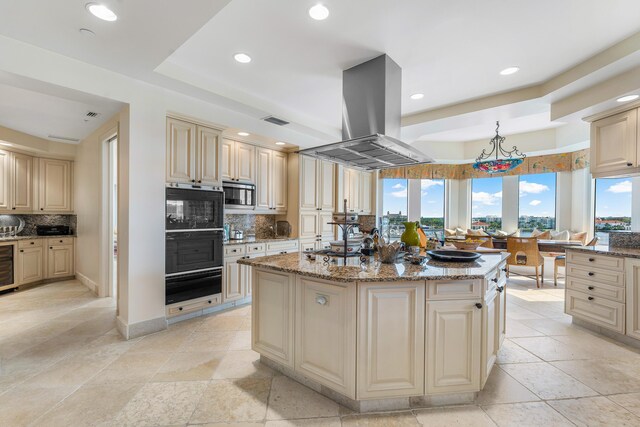 kitchen with island range hood, stainless steel microwave, decorative light fixtures, a kitchen island with sink, and light stone counters