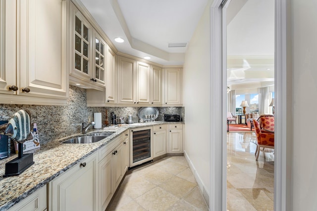 kitchen featuring sink, light stone counters, beverage cooler, decorative backsplash, and cream cabinetry