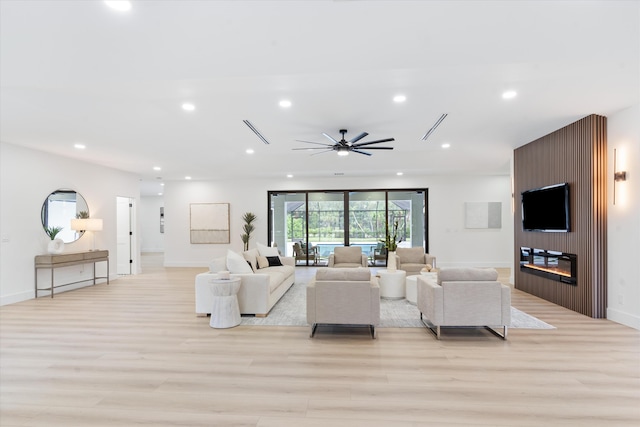 living room featuring ceiling fan, a large fireplace, and light hardwood / wood-style flooring