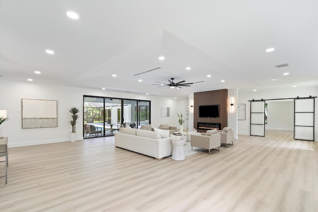 living room with light wood-type flooring, ceiling fan, a barn door, and a fireplace