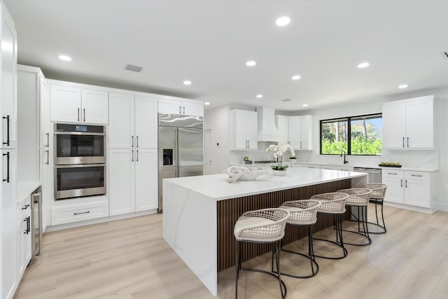 kitchen featuring premium range hood, stainless steel appliances, a kitchen island, white cabinets, and light stone counters