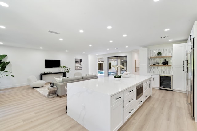 kitchen with stainless steel microwave, a kitchen island, light stone countertops, white cabinets, and beverage cooler