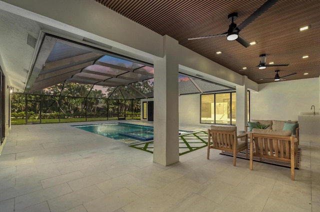 pool at dusk featuring glass enclosure, ceiling fan, an outdoor hangout area, and a patio