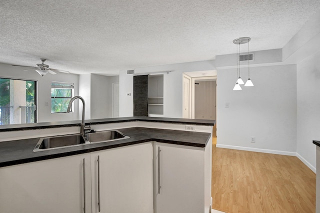 kitchen featuring sink, a textured ceiling, decorative light fixtures, white cabinets, and light wood-type flooring