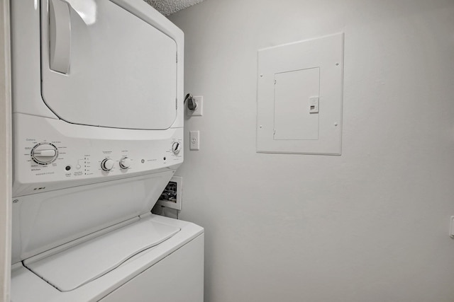 laundry room featuring a textured ceiling, stacked washer / dryer, and electric panel