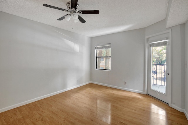 empty room with a wealth of natural light, ceiling fan, a textured ceiling, and light wood-type flooring