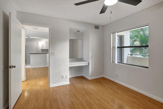 unfurnished bedroom with ceiling fan, built in desk, light hardwood / wood-style floors, and a textured ceiling