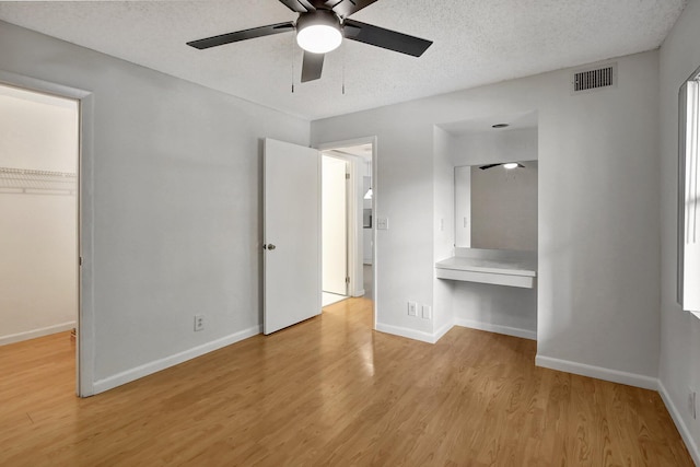 unfurnished bedroom featuring ceiling fan, light hardwood / wood-style floors, a textured ceiling, a closet, and built in desk