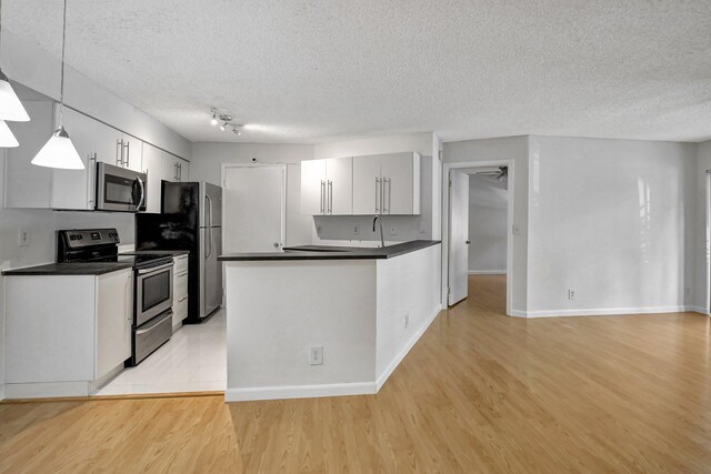 kitchen with a textured ceiling, light wood-type flooring, stainless steel appliances, and hanging light fixtures