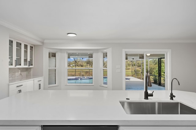 kitchen with backsplash, crown molding, white cabinetry, and sink