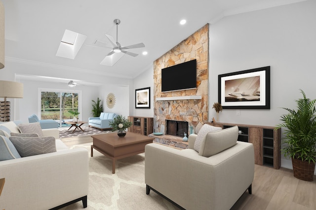 living room with a skylight, ceiling fan, a stone fireplace, crown molding, and light wood-type flooring