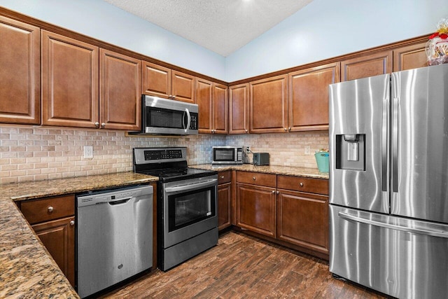 kitchen featuring appliances with stainless steel finishes, vaulted ceiling, light stone counters, and dark wood-type flooring