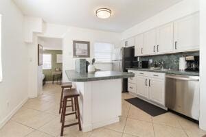 kitchen with decorative backsplash, stainless steel dishwasher, light tile patterned floors, white cabinets, and a breakfast bar area