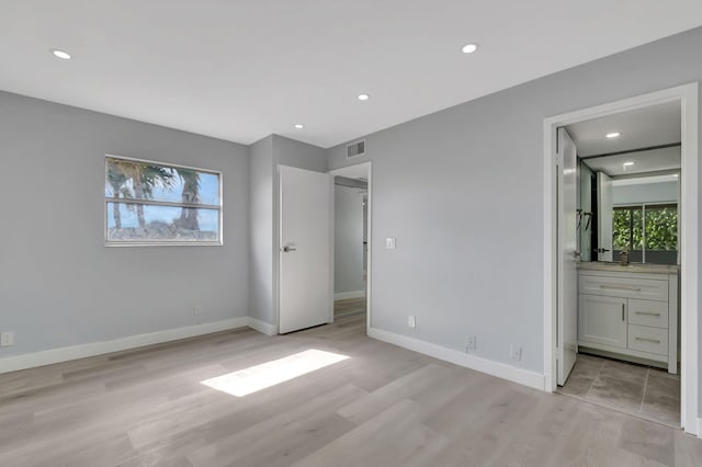 unfurnished bedroom featuring ensuite bathroom and light wood-type flooring