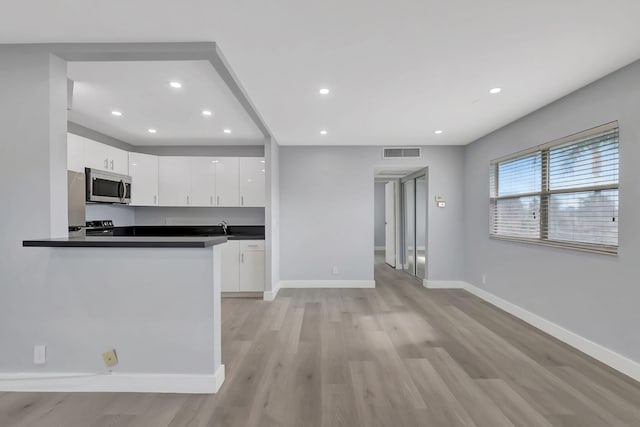 kitchen with white cabinets, light wood-type flooring, kitchen peninsula, and sink